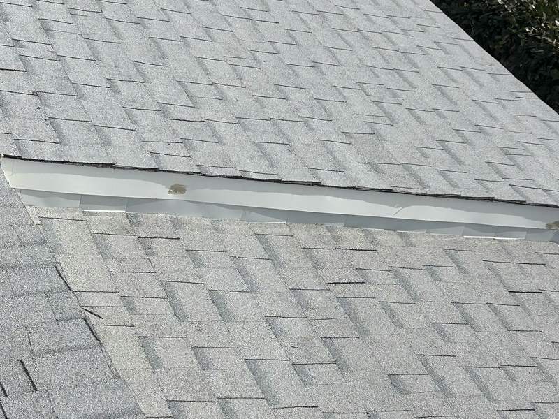 Close roof-level view of a finished light-gray asphalt shingle plane and flashing detail.