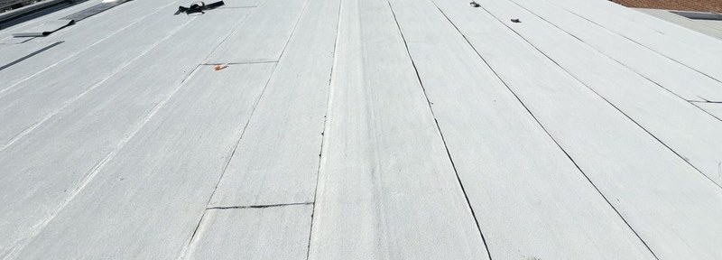 White coated low-slope roof field with evenly spaced parallel seams and dark lines along each seam.