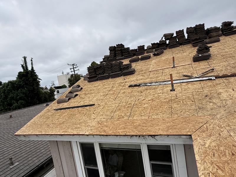 Broad sloped roof covered with exposed wood sheathing and staged roofing materials.